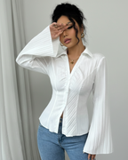 Woman wearing a white blouse with bell sleeves against a gray curtain background