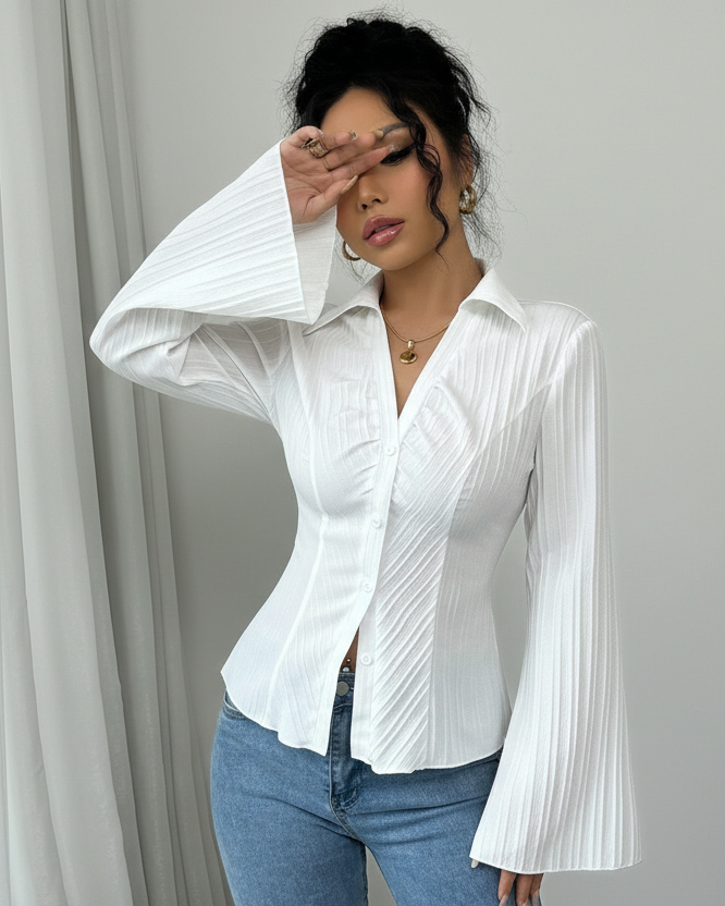 Woman wearing a white blouse with bell sleeves against a gray curtain background