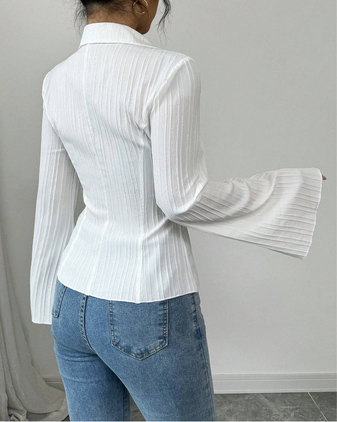 Person wearing a white pleated blouse and blue jeans against a gray background