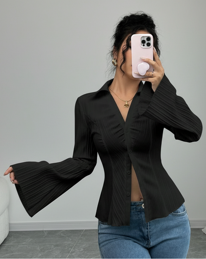 Person wearing a black pleated blouse and blue jeans, standing against a plain background.
