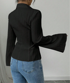 Person wearing a black pleated blouse and blue jeans against a plain background